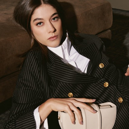 Woman in a pinstripe suit holding a beige handbag on a couch.