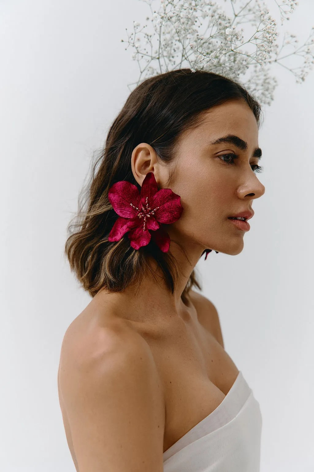 Woman wearing a bright pink flower earring against a white background