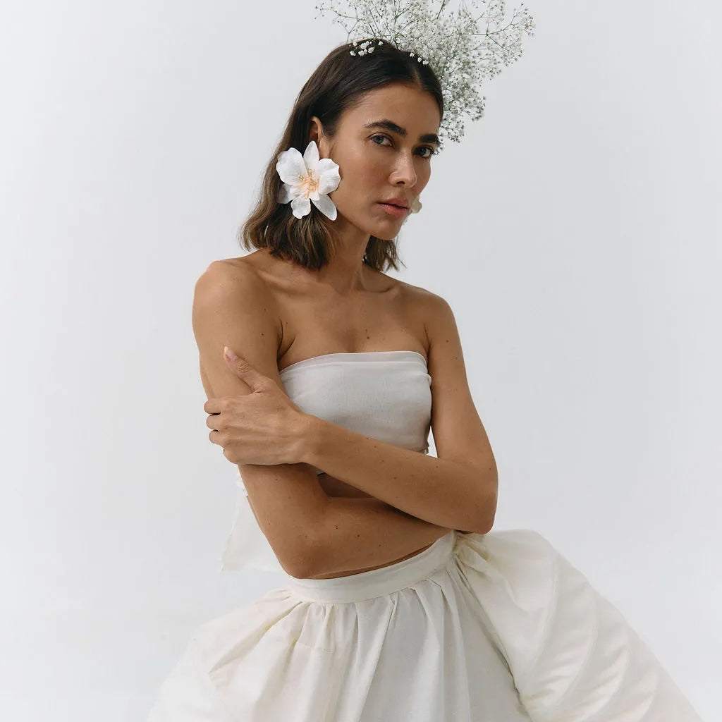 Woman wearing a strapless white dress with a floral headpiece against a plain background