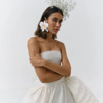 Woman wearing a strapless white dress with a floral headpiece against a plain background