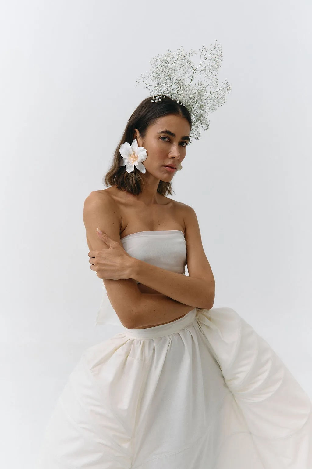 Woman wearing a strapless white dress with a floral headpiece against a plain background