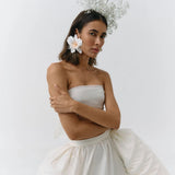 Woman wearing a strapless white dress with a floral headpiece against a plain background