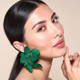 Woman wearing green floral earrings against a beige background