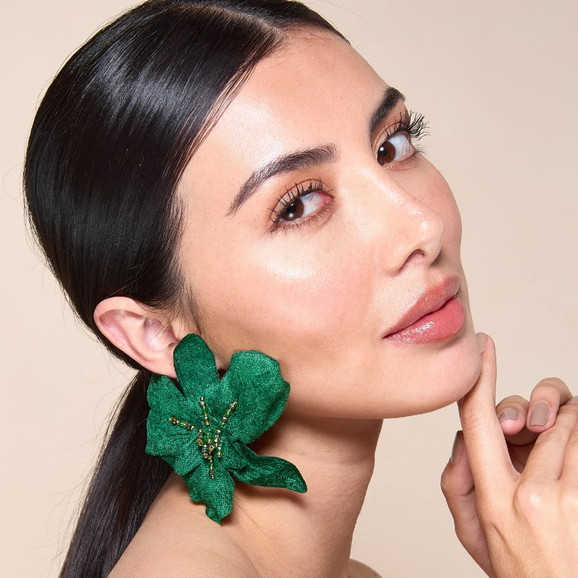Woman wearing green floral earrings against a beige background