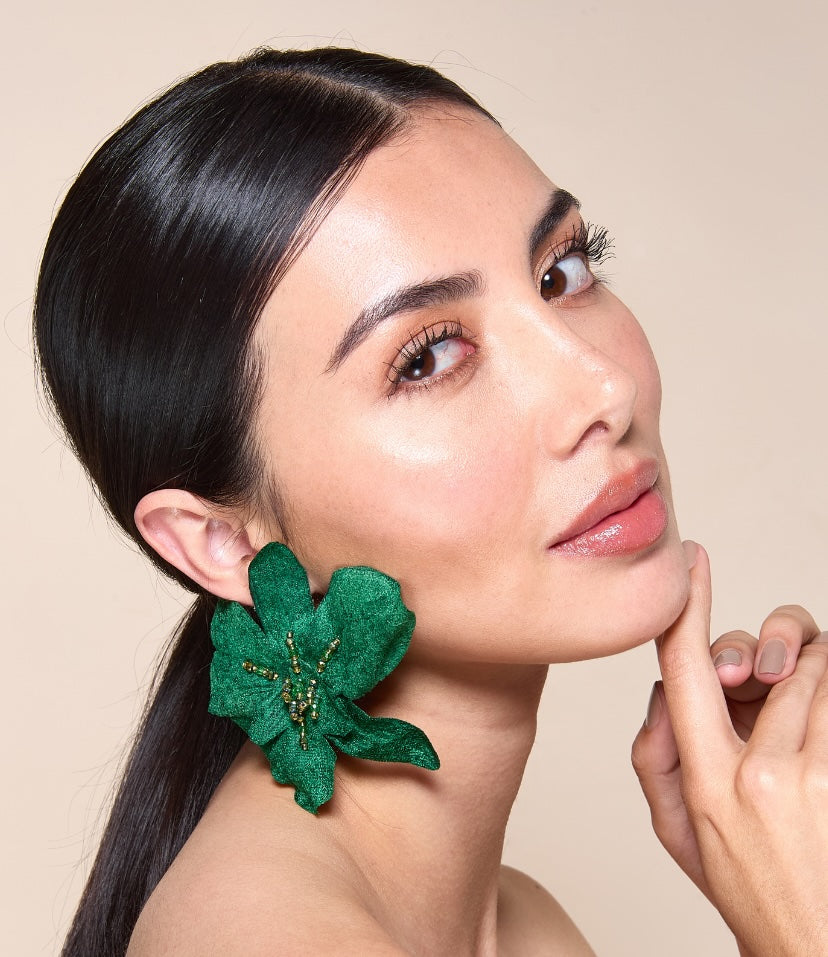 Woman wearing green floral earrings against a beige background