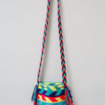 A small handmade Wayuu crossbody bag with a geometric pattern, featuring a wide woven strap and a flat tassel closure.