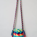 A small handmade Wayuu crossbody bag with a geometric pattern, featuring a wide woven strap and a flat tassel closure.