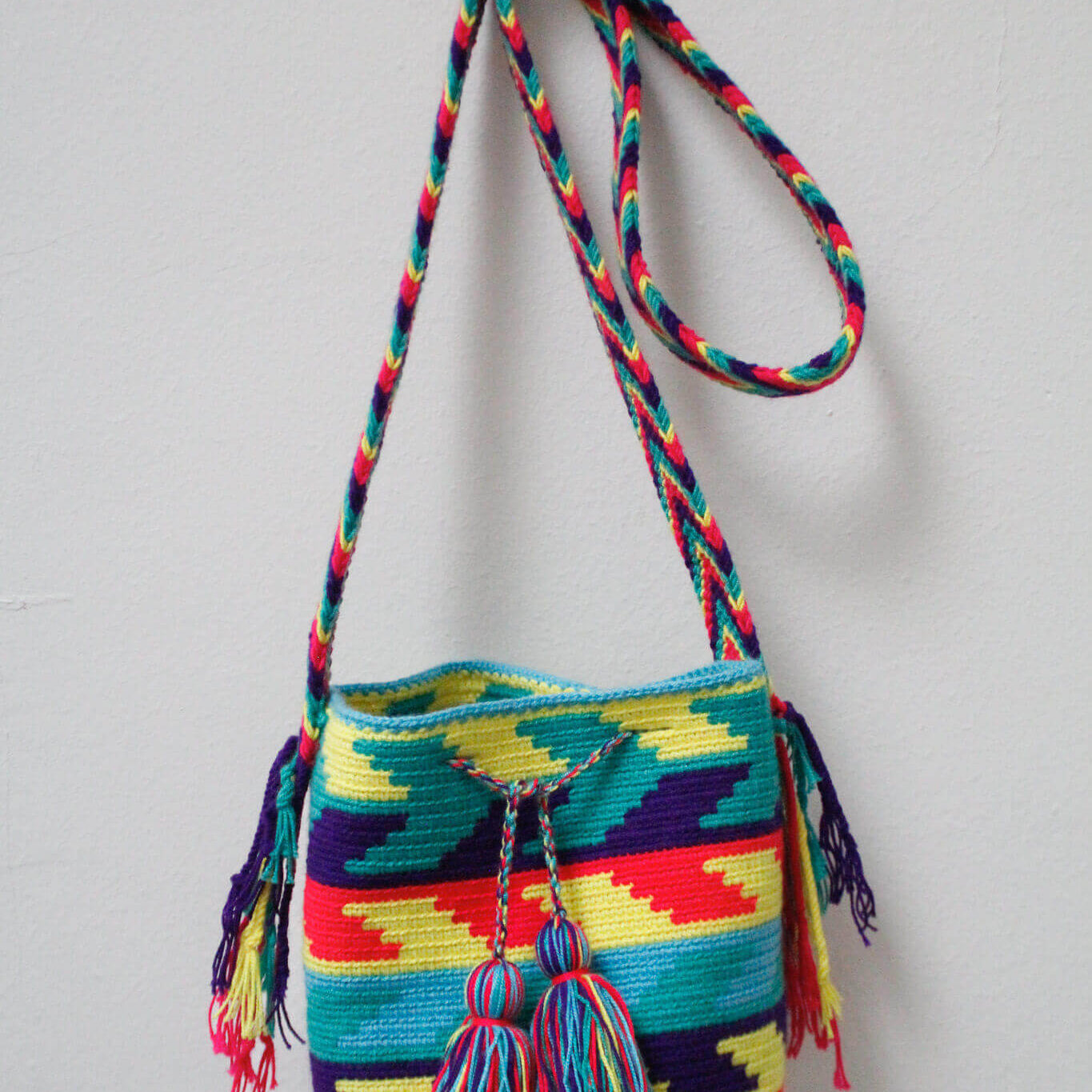 A small handmade Wayuu crossbody bag with a geometric pattern, featuring a wide woven strap and a flat tassel closure.