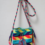 A small handmade Wayuu crossbody bag with a geometric pattern, featuring a wide woven strap and a flat tassel closure.