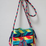 A small handmade Wayuu crossbody bag with a geometric pattern, featuring a wide woven strap and a flat tassel closure.