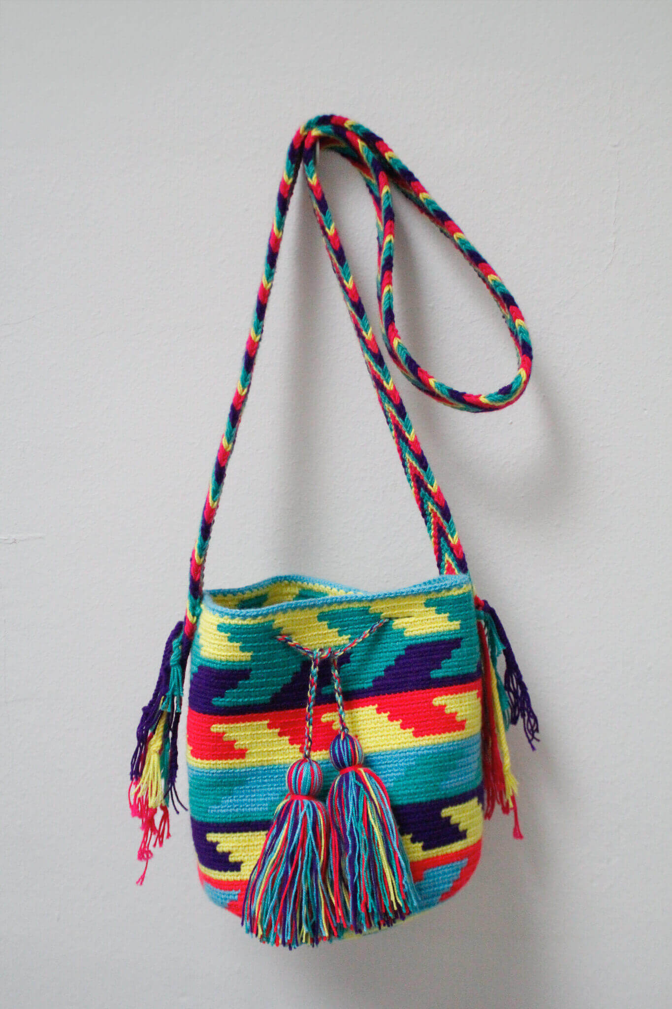 A small handmade Wayuu crossbody bag with a geometric pattern, featuring a wide woven strap and a flat tassel closure.