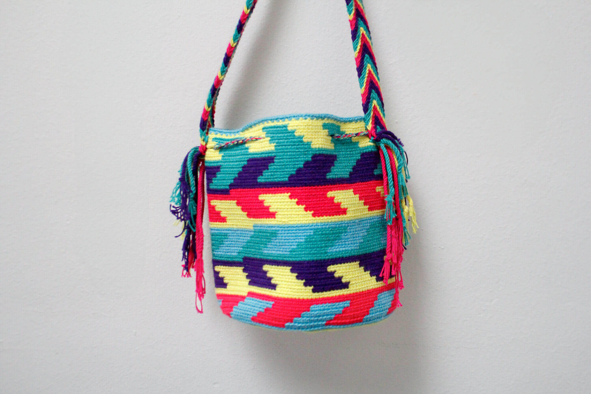 A small handmade Wayuu crossbody bag with a geometric pattern, featuring a wide woven strap and a flat tassel closure.