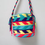 A small handmade Wayuu crossbody bag with a geometric pattern, featuring a wide woven strap and a flat tassel closure.