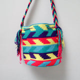 A small handmade Wayuu crossbody bag with a geometric pattern, featuring a wide woven strap and a flat tassel closure.