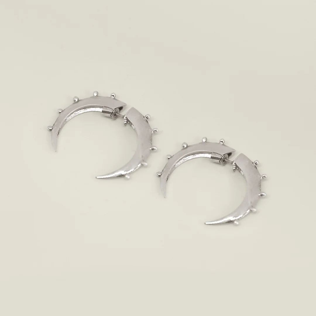 Silver crescent hoop earrings with small studs on a beige background. 
