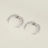 Silver crescent hoop earrings with small studs on a beige background. 