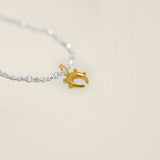 Gold horse shoe charm on a silver chain against a beige background