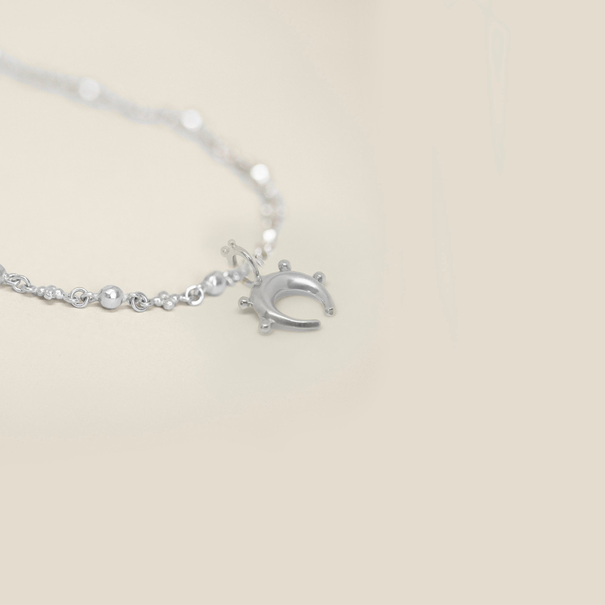 Small sterling silver horseshoe pendant with sphere detail on a neutral background
