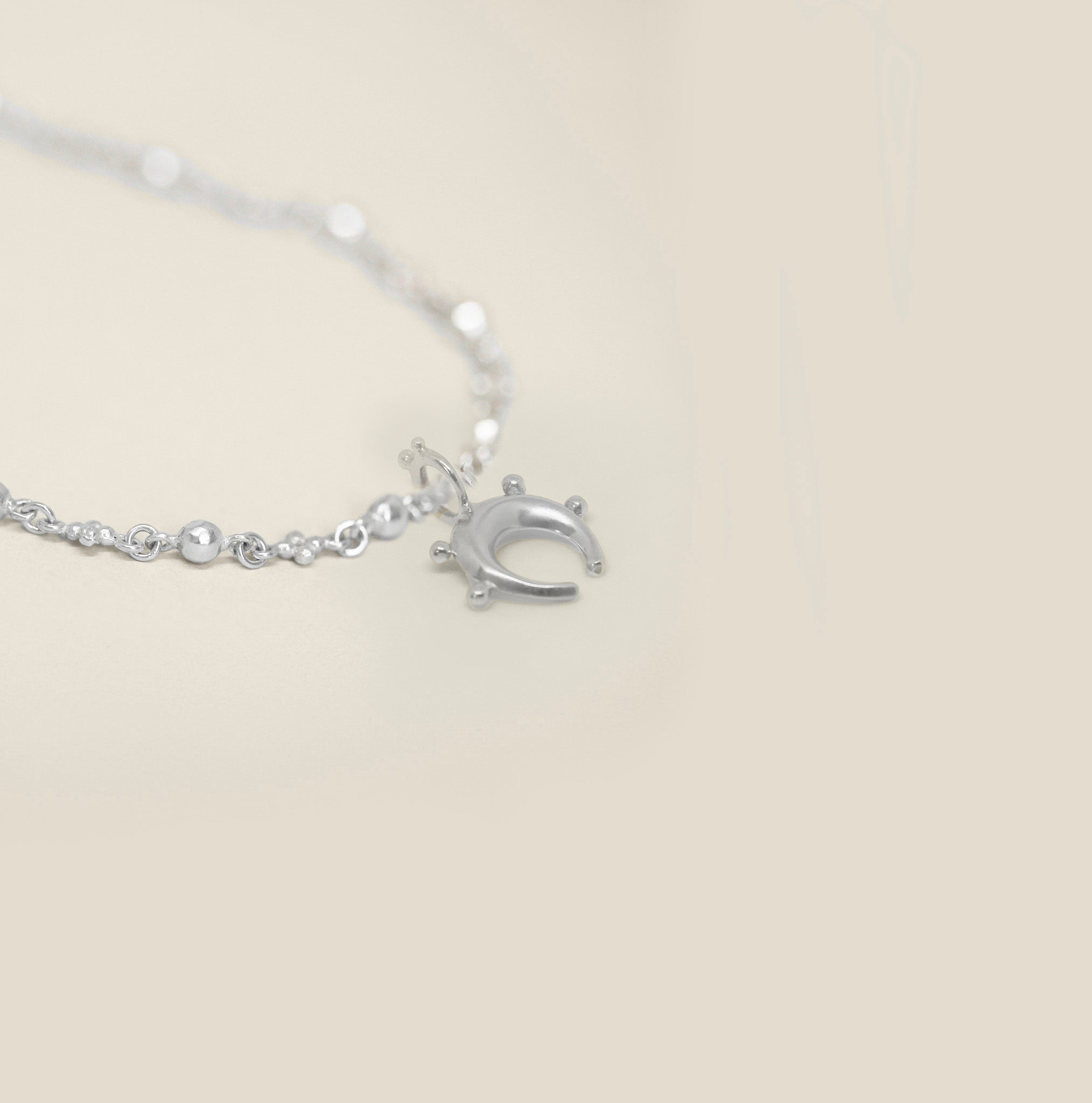 Small sterling silver horseshoe pendant with sphere detail on a neutral background