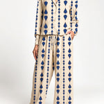 A woman modeling a two-piece set with a beige base and a blue geometric diamond pattern, featuring a long-sleeve button-up top and matching wide-leg pants.