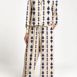 A woman modeling a two-piece set with a beige base and a blue geometric diamond pattern, featuring a long-sleeve button-up top and matching wide-leg pants.