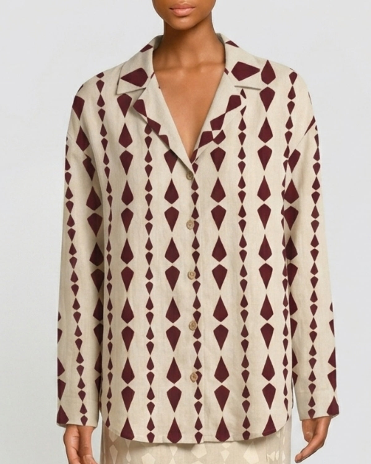 A model wearing a long-sleeve button-front shirt jacket with a cream base and a dark burgundy geometric diamond pattern.