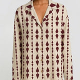 A model wearing a long-sleeve button-front shirt jacket with a cream base and a dark burgundy geometric diamond pattern.