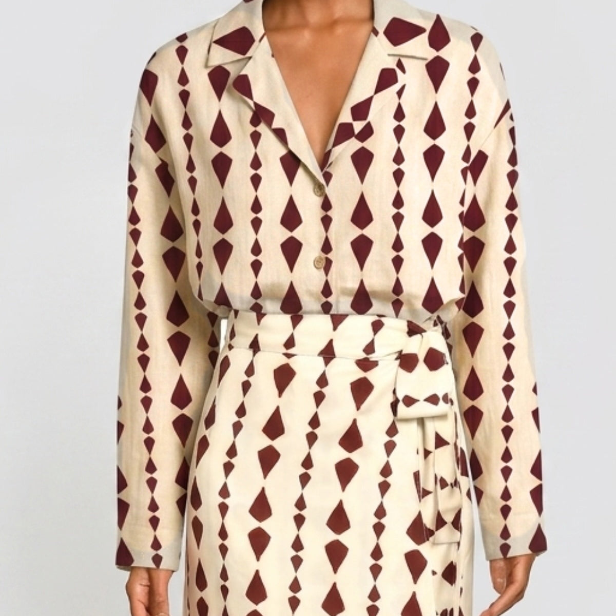 A model wearing a long-sleeve collared shirt dress with a cream base and a dark burgundy geometric diamond pattern, featuring a matching tie belt.