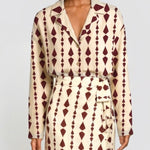 A model wearing a long-sleeve collared shirt dress with a cream base and a dark burgundy geometric diamond pattern, featuring a matching tie belt.