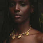 Woman wearing a gold necklace with green gemstones against a dark background