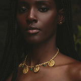 Woman wearing a gold necklace with green gemstones against a dark background