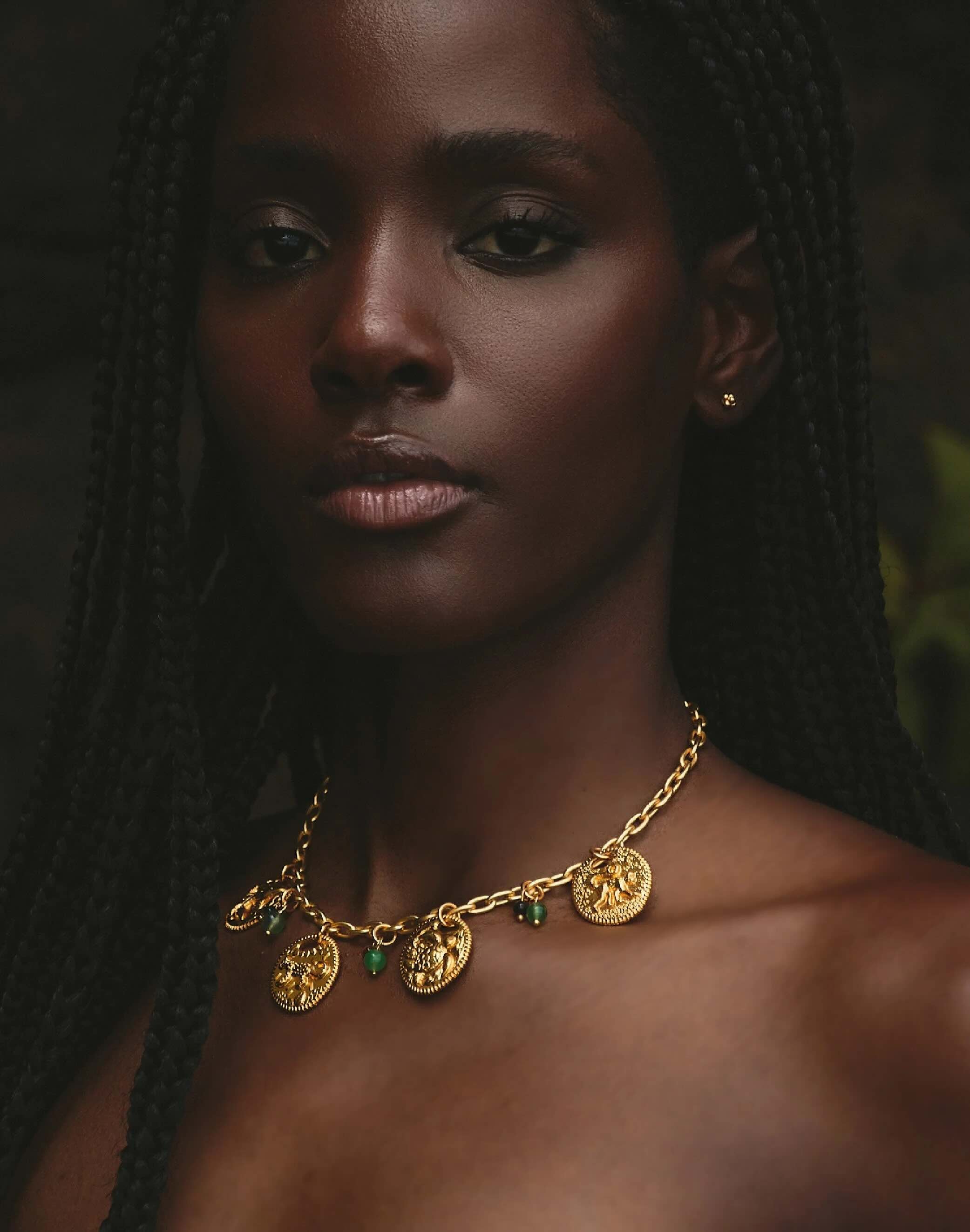 Woman wearing a gold necklace with green gemstones against a dark background