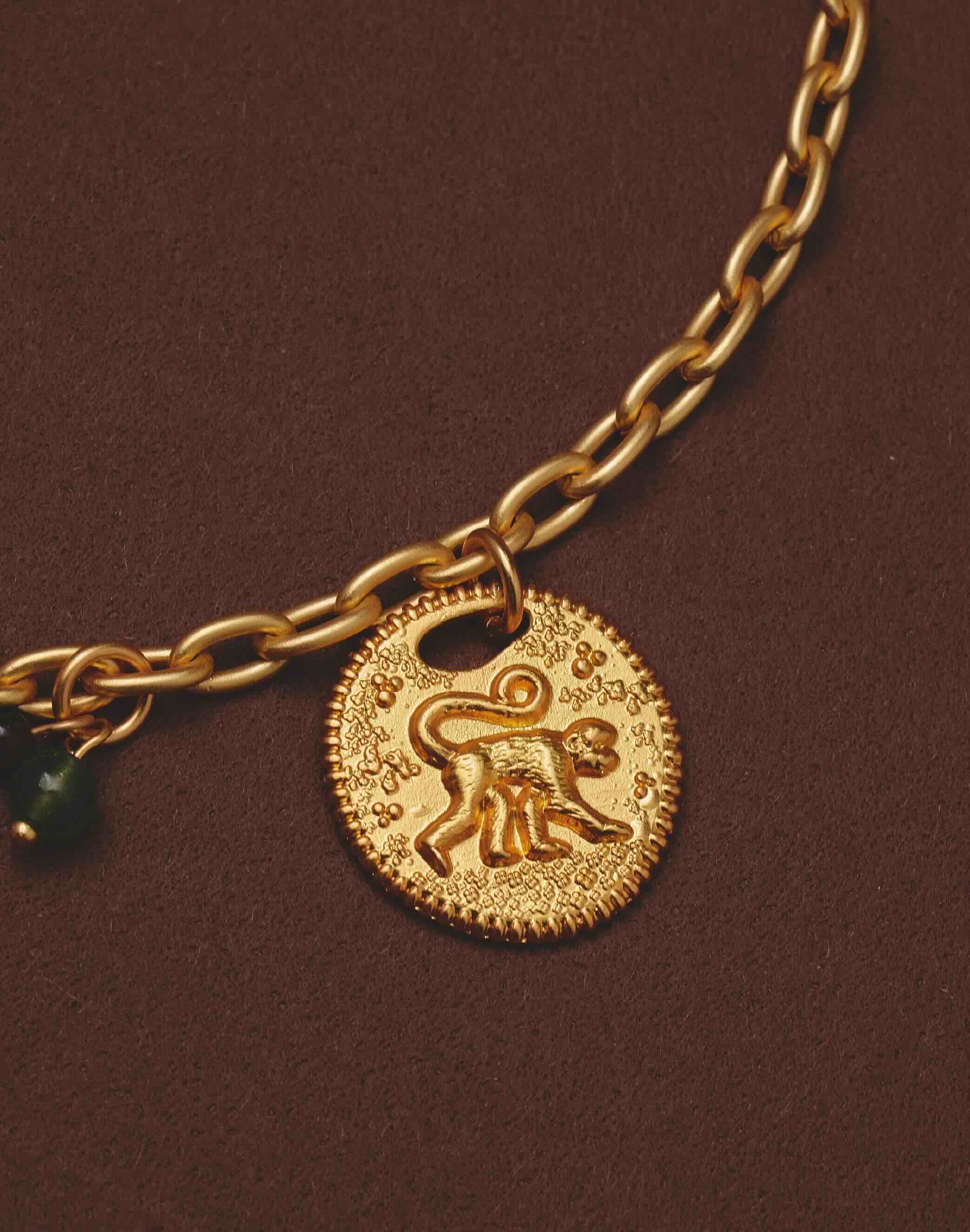 Gold necklace close-up with a monkey pendant on a brown background