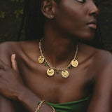 Woman wearing a gold necklace and bracelet with green accents against a dark background