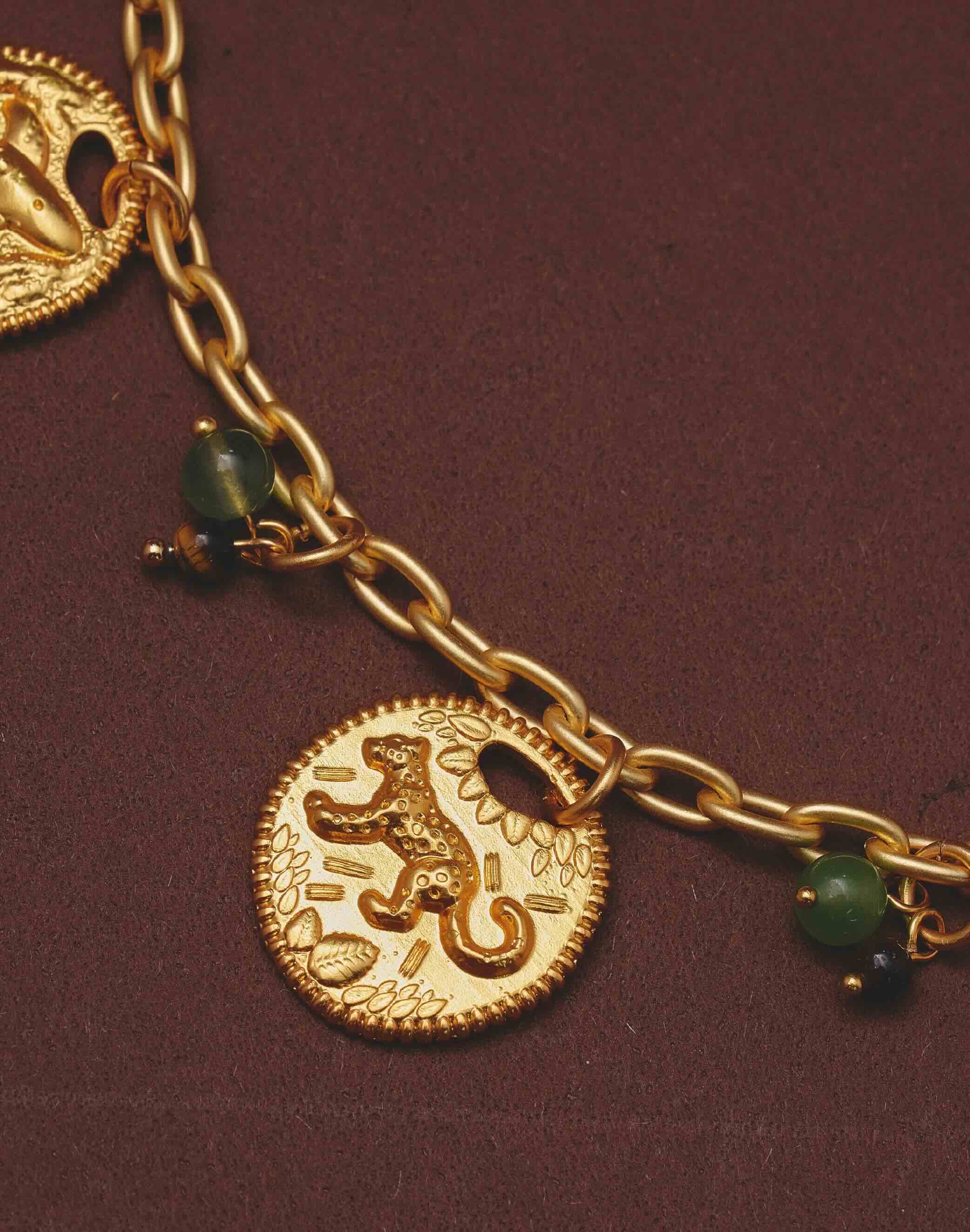 Close up of a necklace with a lion charm and green beads on a dark background