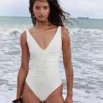 Woman in a white swimsuit standing on a beach with ocean waves in the background