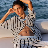 Woman lounging on a boat wearing a patterned outfit with ocean in the background.