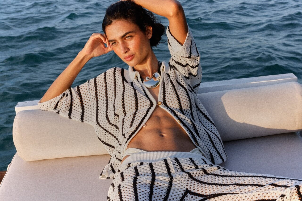 Woman lounging on a boat wearing a patterned outfit with ocean in the background.