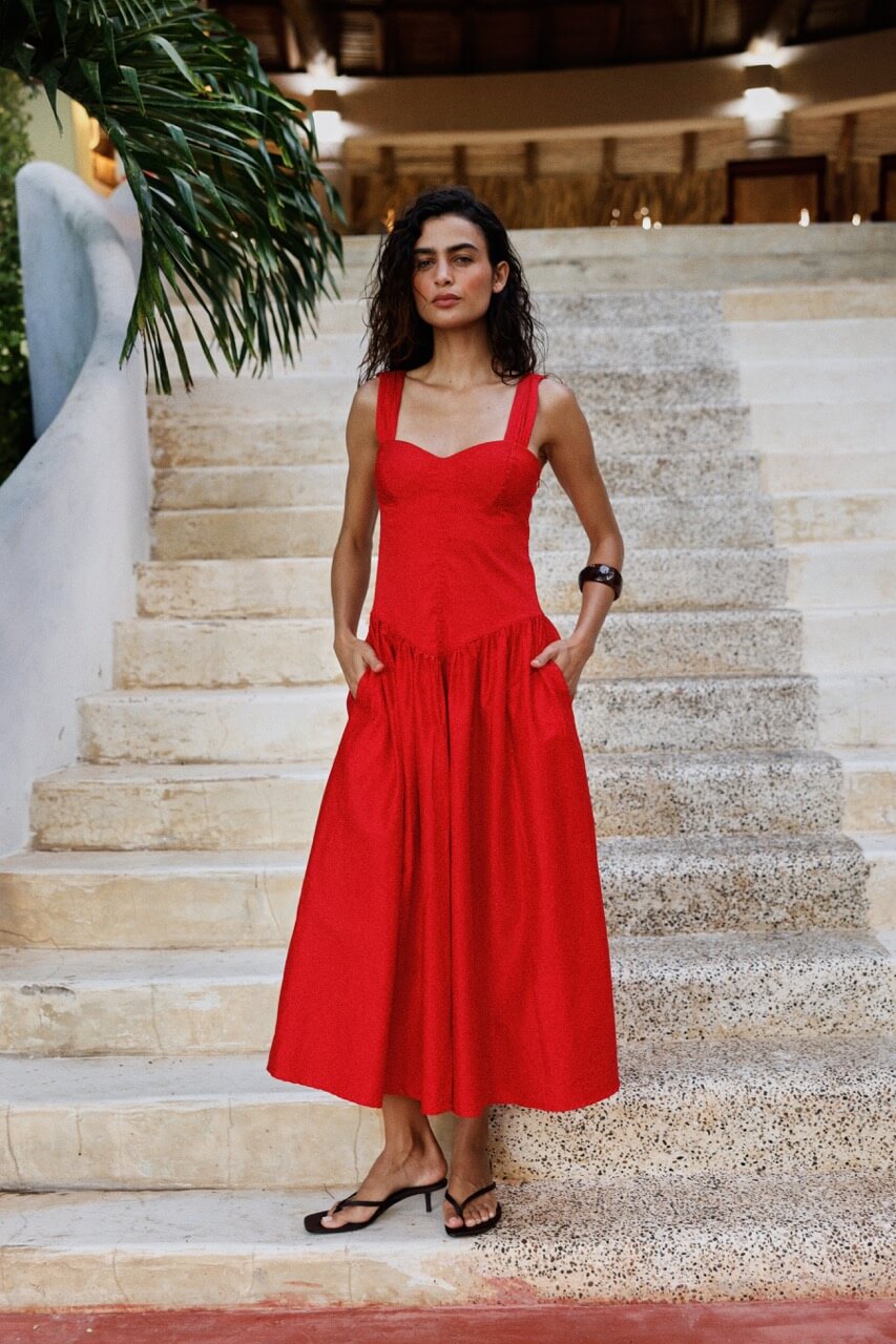 Woman in a red dress standing on stone steps with greenery in the background. 