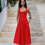 Woman in a red dress standing on stone steps with greenery in the background. 