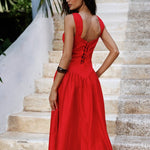 Woman in a red dress standing on stone steps with greenery in the background.