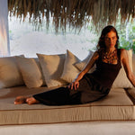 Woman sitting on a large cushioned couch wearing a black dress from Encantadore. 