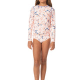 A young girl modeling a long-sleeve swim shirt and matching swim briefs with a white base and a blue and orange abstract pattern, set against a plain white background.