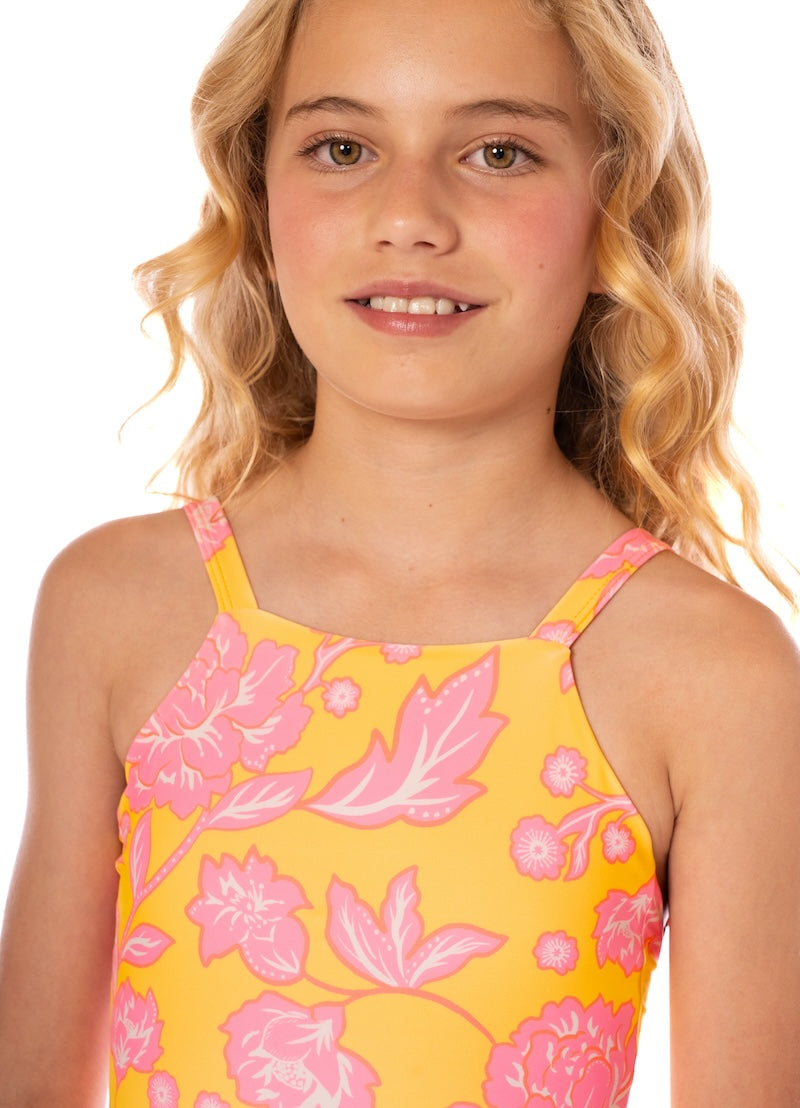 Young girl wearing a yellow floral dress with pink flowers on a white background.
