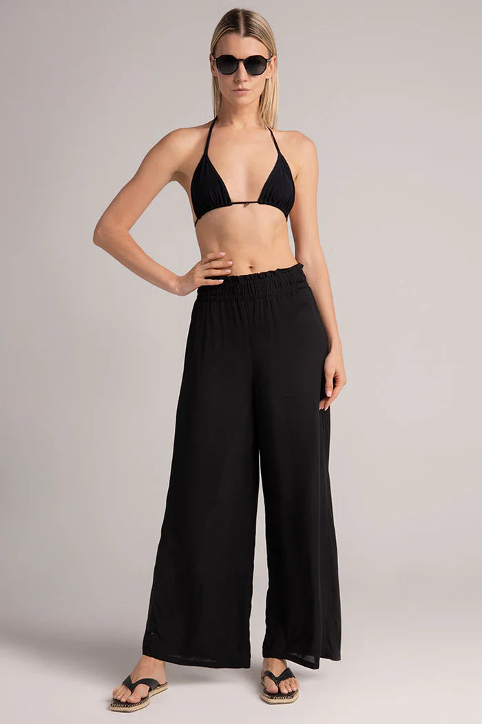 Woman wearing a black bikini top and wide-leg pants on a plain background.