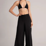 Woman wearing a black bikini top and wide-leg pants on a plain background.