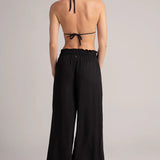 Woman wearing a black halter bikini top and wide-leg pants on a plain background.