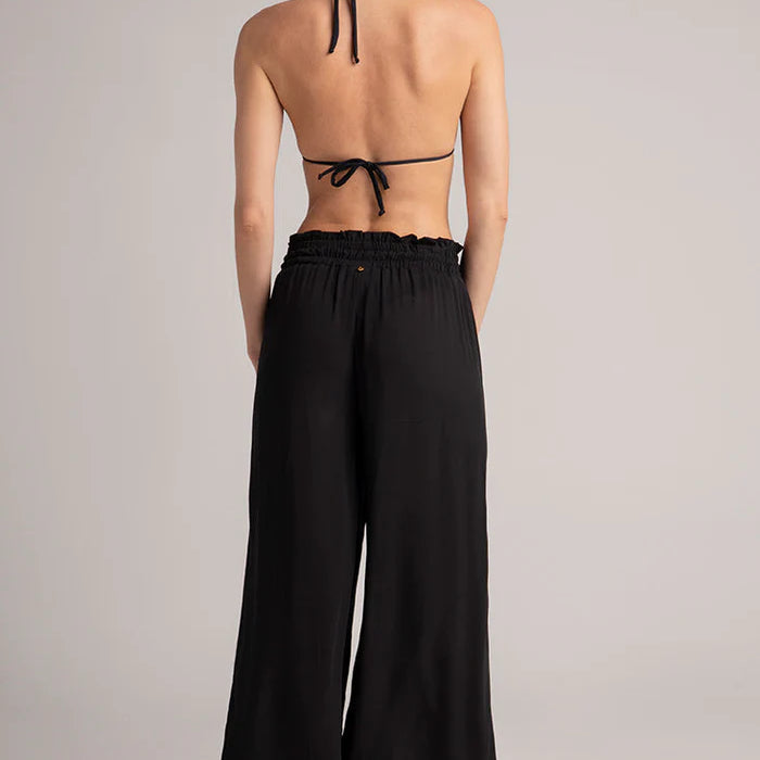 Woman wearing a black halter bikini top and wide-leg pants on a plain background.
