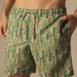 Green and orange fish patterned swim shorts worn by a person on a neutral background.