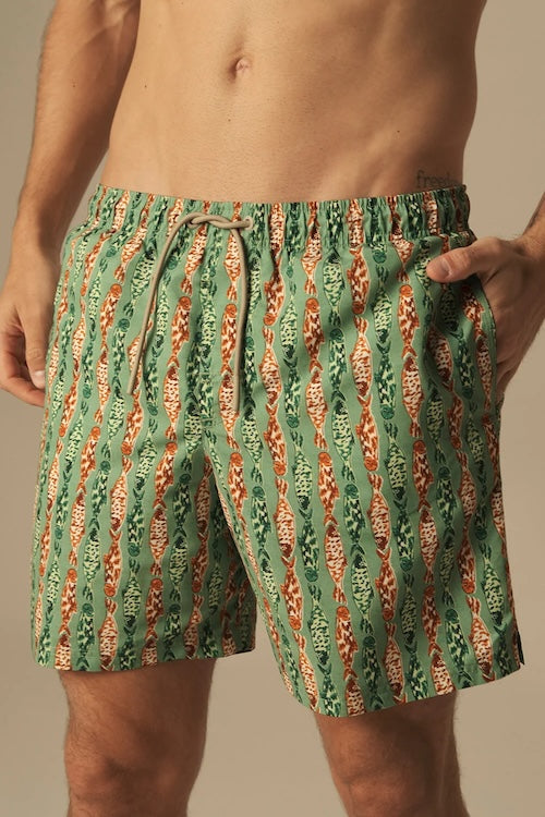 Green and orange fish patterned swim shorts worn by a person on a neutral background.